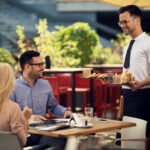 Happy waiter serving a meal to a couple during lunch time in a restaurant.